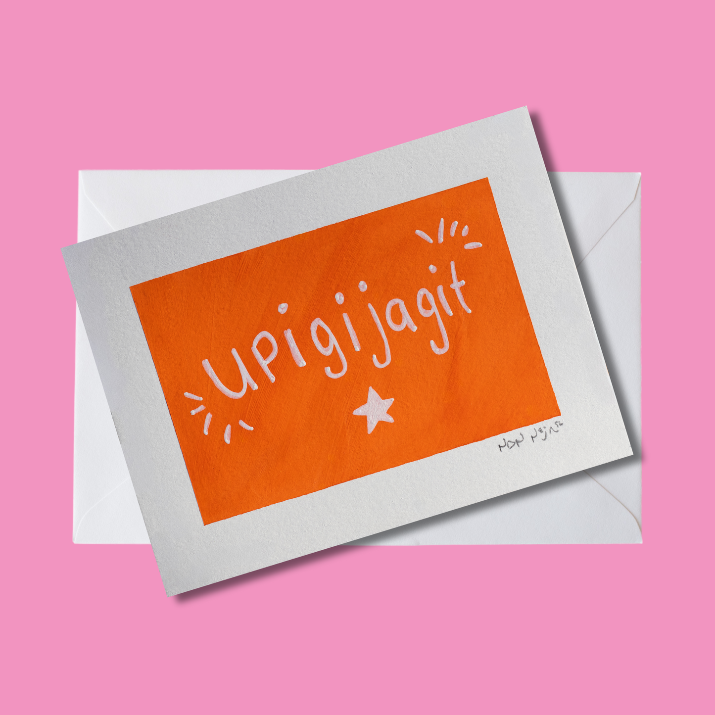 Hand-painted artwork titled ‘Upigijagit,’ featuring the phrase meaning ‘I’m proud of you’ written in cheerful white lettering on a bold orange background. A small white star sits below the text, with playful white accent marks radiating from the sides. The piece is tilted slightly and framed by a white border, set against a bright pink background and white envelope that adds warmth and energy to the composition.