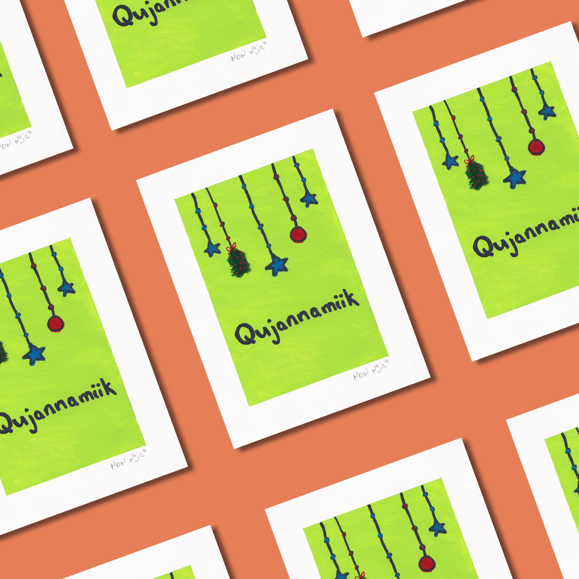 Flat lay of hand-painted ‘Qujannamiik’ greeting cards arranged on a coral background. Each card features hanging blue stars and ornaments above the Inuktitut word ‘Qujannamiik,’ meaning thank you.